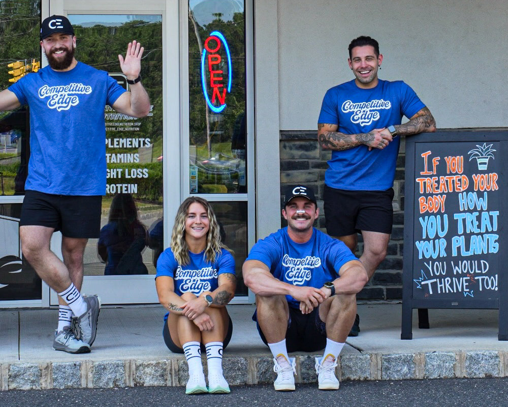 Four people in blue shirts posing in front of a store named 'Competitive Edge Nutrition'.